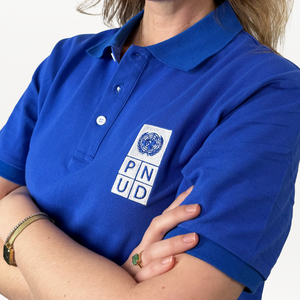 A close-up of a woman wearing a blue polo shirt with a white and blue PNUD logo on the right.