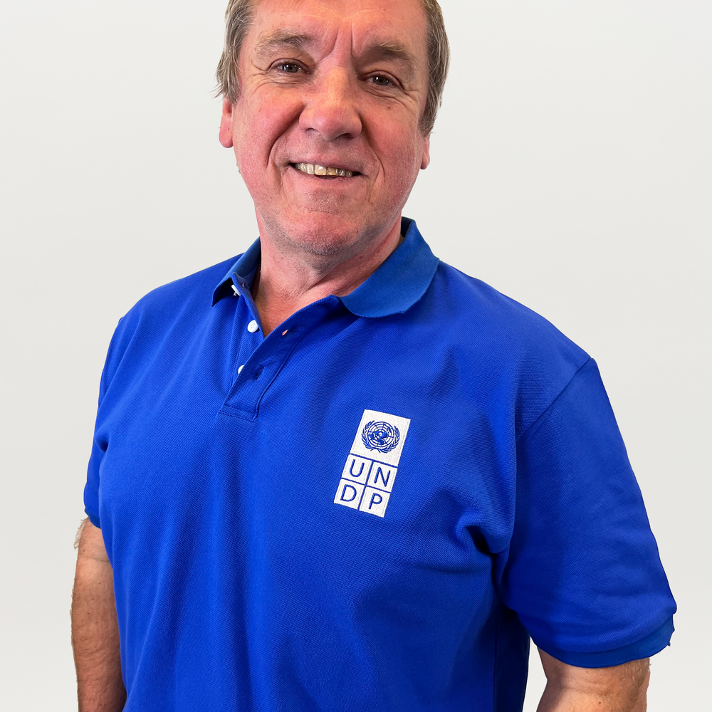 A man wearing a blue polo shirt with a white and blue UNDP logo on the right. 